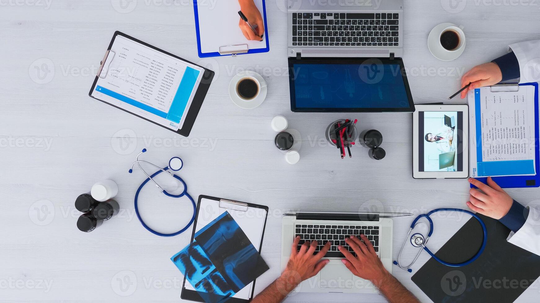 Top view of resident physicians advising with doctor using videocall sitting on desk in clinic with medical equipment. Talking with specialist on videomeeting online conference on copy space, flat lay photo