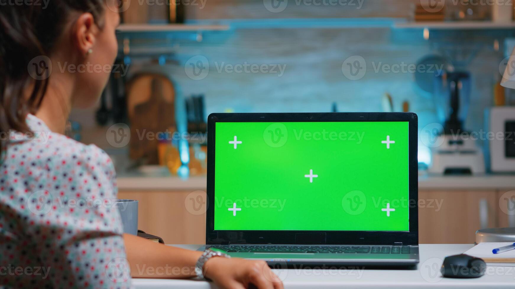 Remote employee looking at chroma key sitting in home kitchen late at night. Business woman watching desktop laptop display with green mockup, screen, during night time working overtime. photo