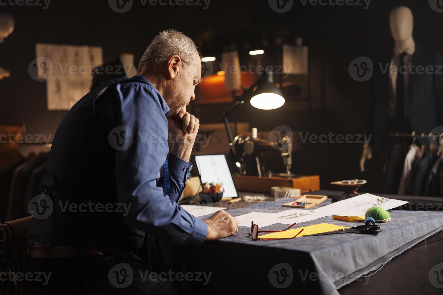 Elderly suitmaker overthinking comissioned business suit required by customer. Old experienced couturier working on sartorial bespoken clothing designs in tailoring studio workspace photo