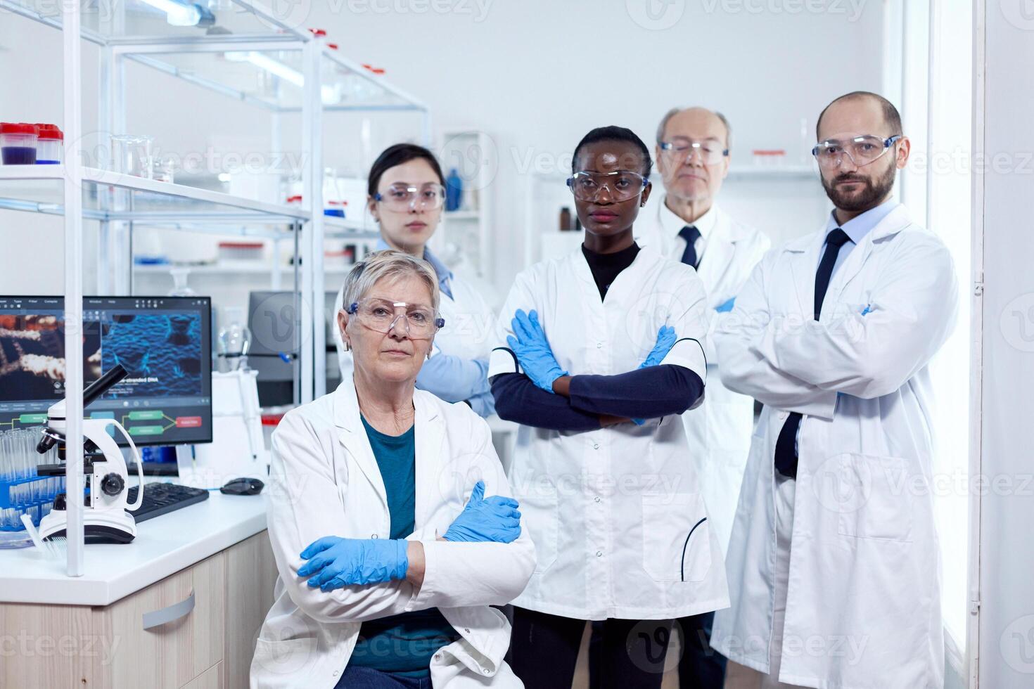 Portrait of head scientific project ar her research team holding arms crossed at workplace. African healthcare scientist in biochemistry laboratory wearing sterile equipment. photo