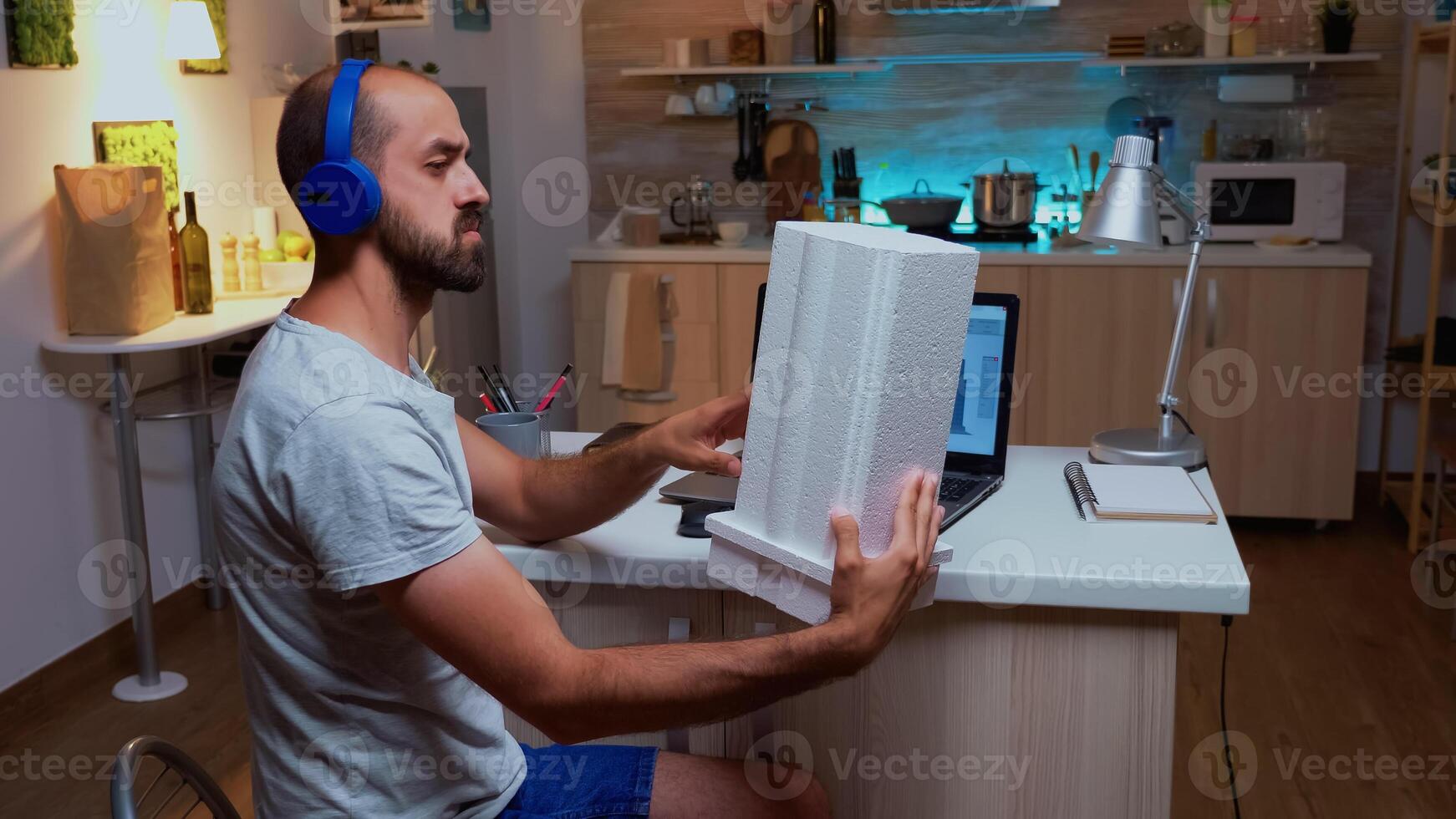 Architect holding building model while working on a project during night in home. Industrial male employee studying prototype idea on personal computer showing cad software on device display photo