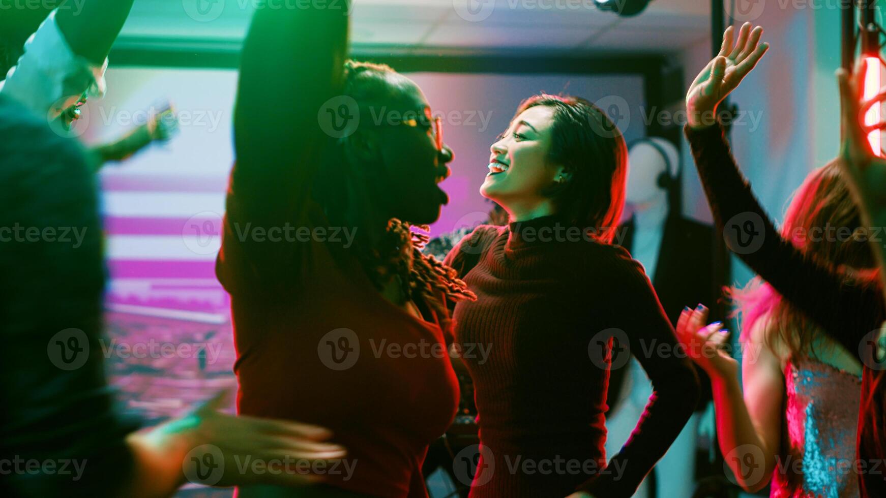 Modern people jumping around at club, having fun dancing on electronic funky music at party. Young men and women enjoying nightlife on dance floor, discotheque performance. Tripod shot. photo