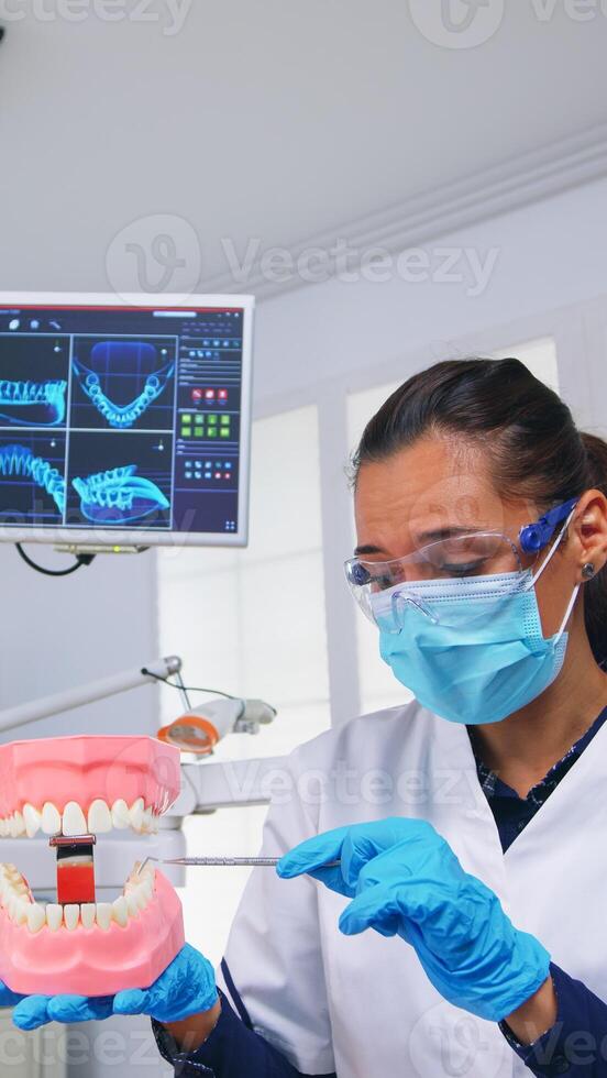 Patient pov of dentist showing correct way of cleaning teeth wearing in dental office using teeth medical skeleton accessory. Stomatolog wearing protection mask during heatlhcare check photo