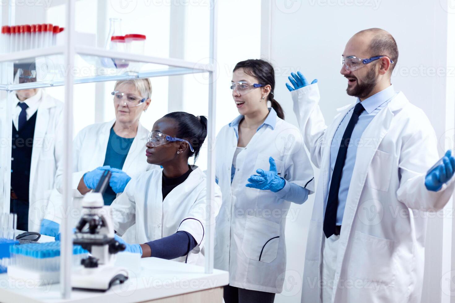 Group of scientists with diverse race working to find a cure vor virus during pandemic. Black healthcare researcher in biochemistry laboratory wearing sterile equipment. photo