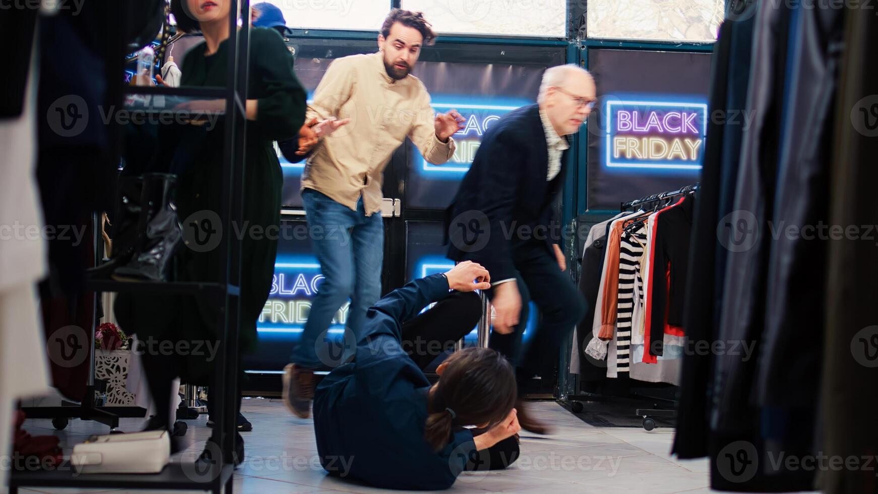Customer falling in clothing store, getting hurt by crazy anxious crowd of people pushing red tape. Careless shoppers fighting with security guard, black friday madness. Tripod shot. photo