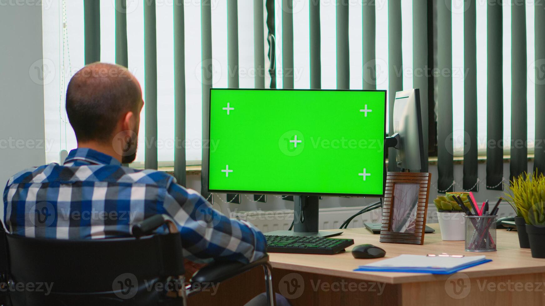 Immobilized businessman in wheelchair using computer with chroma key for videomeeting. Handicapped disabled freelancer looking at pc with green screen, mockup, key talking with remotely colleagues photo