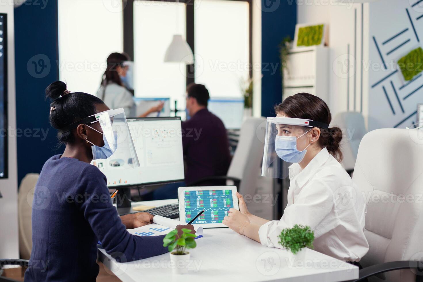 Multiethnic people discussing the charts and graphs wearing face mask during covid19. Diverse group of business people working and communicating together in creative office with new normal, respecting social distance. photo