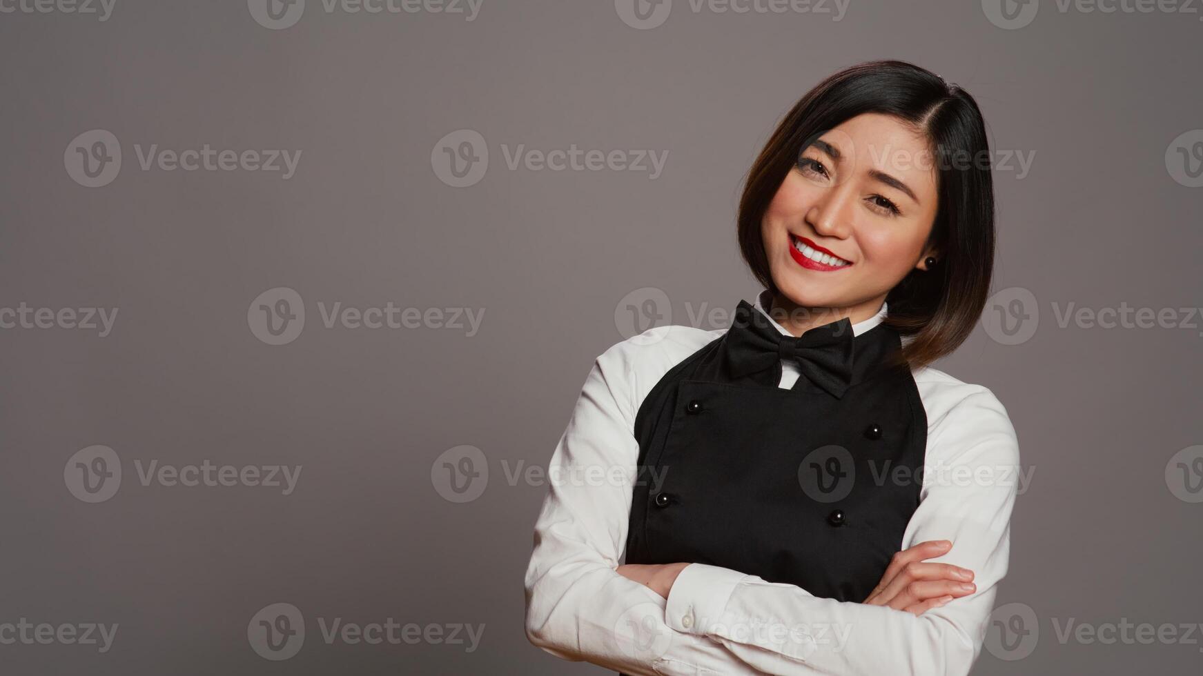 Asian restaurant employee serving clients at tables, offering luxury catering services with tray on camera. Waitress working in gourmet industry, wearing apron and bow in studio. Camera B. photo