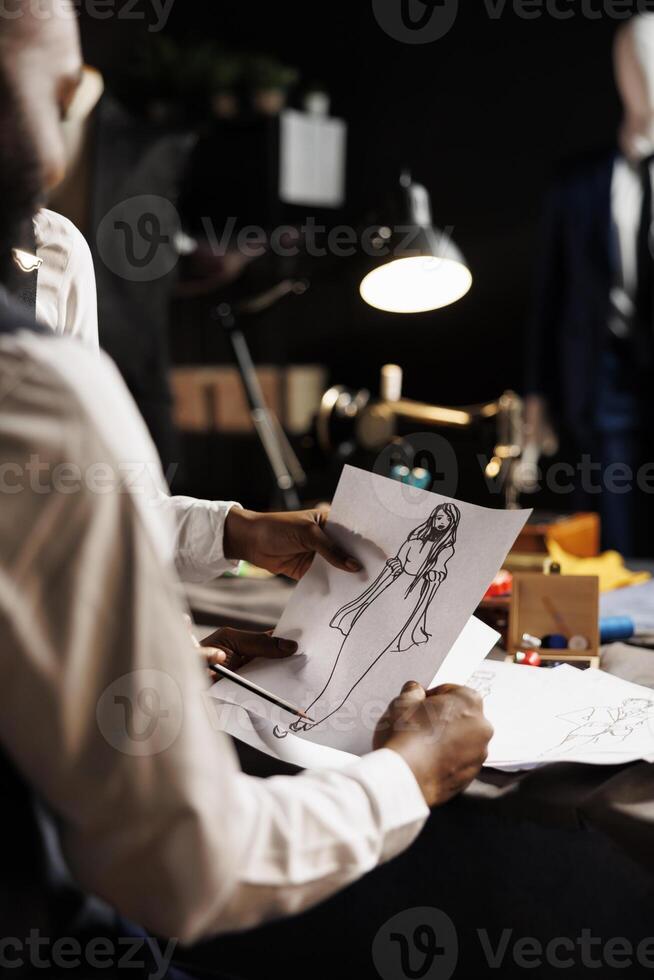 Tailoring studio workspace collegues brainstorming best adjustments to be made on premium quality bespoke dress to be made for client. Dressmakers using sketch drawing to design sartorial garment photo