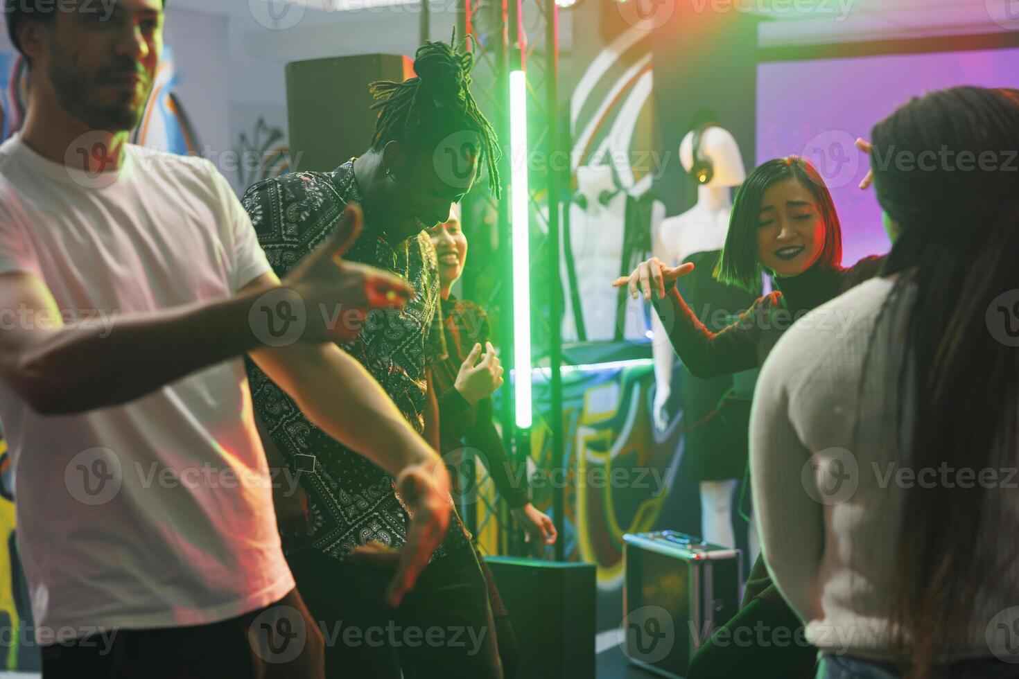 Diverse friends group dancing while attending discotheque party in nightclub. Young men and women clubbers having fun and making moves to electronic music beats on dancefloor in club photo