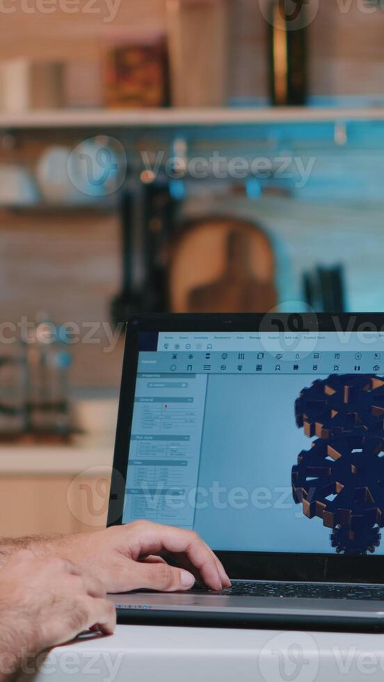 Man architect with wireless headset using laptop while working at home at night sitting in the kitchen. Industrial employee studying prototype idea on personal computer showing cad software on display photo