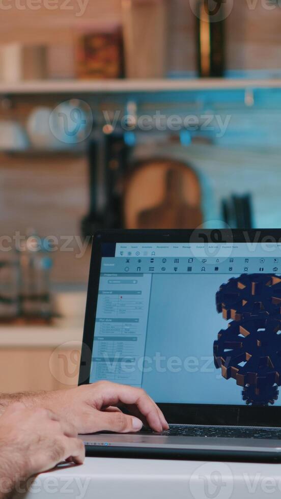 Man architect with wireless headset using laptop while working at home at night sitting in the kitchen. Industrial employee studying prototype idea on personal computer showing cad software on display photo