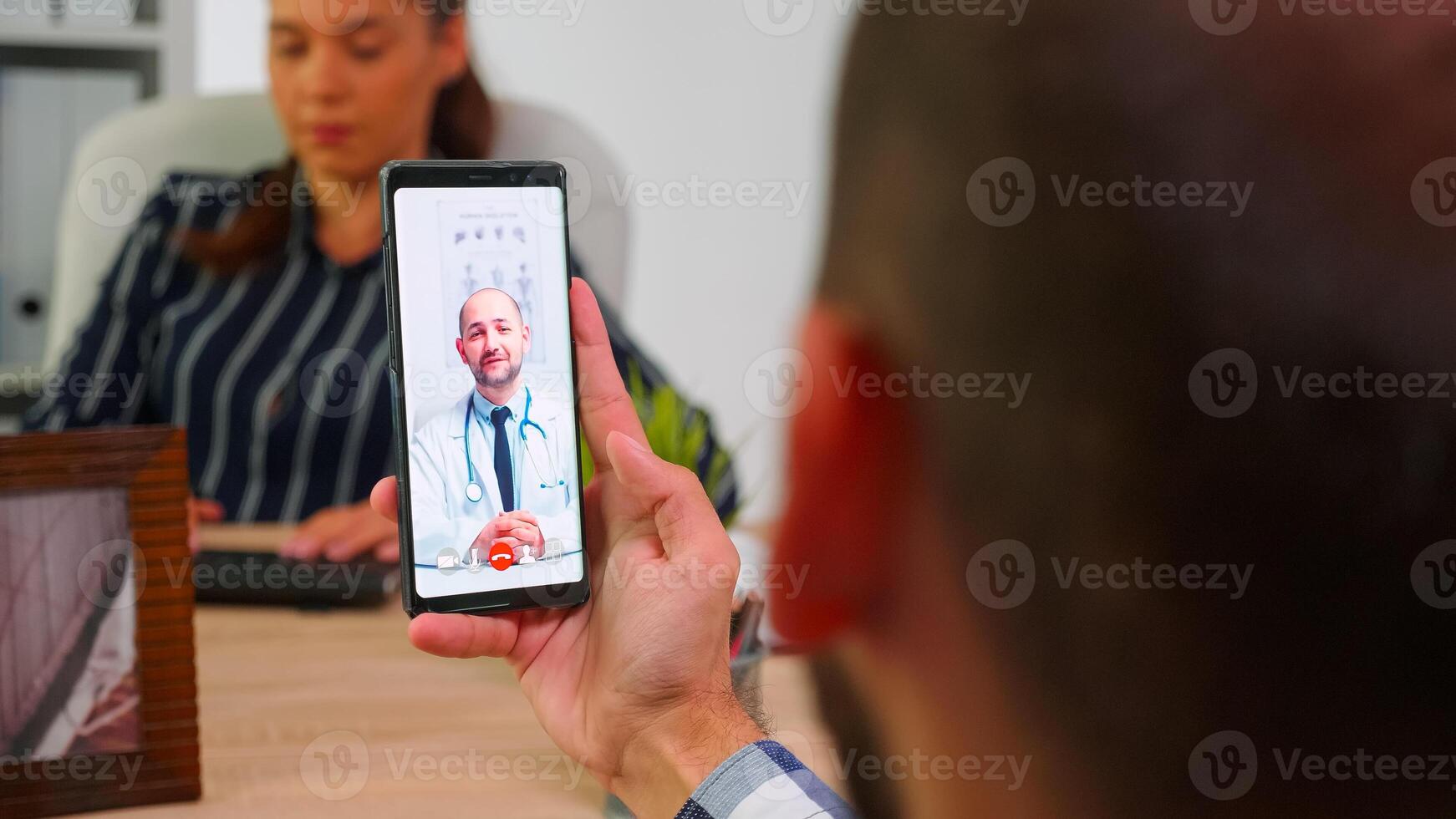 Disabled businessman talking on video call with doctor in work time sitting in wheelchair in modern company office using smartphone. Remotely medic advising freelancer using modern technology photo