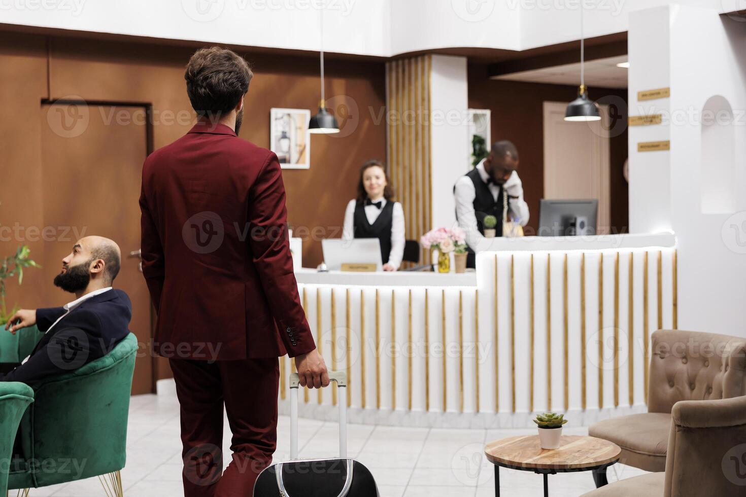 Formal guest enter reception area, carrying suitcase at front desk to do check in process. Businessman in suit with luggage trolley travelling for work purposes, staff ensuring pleasant stay. photo