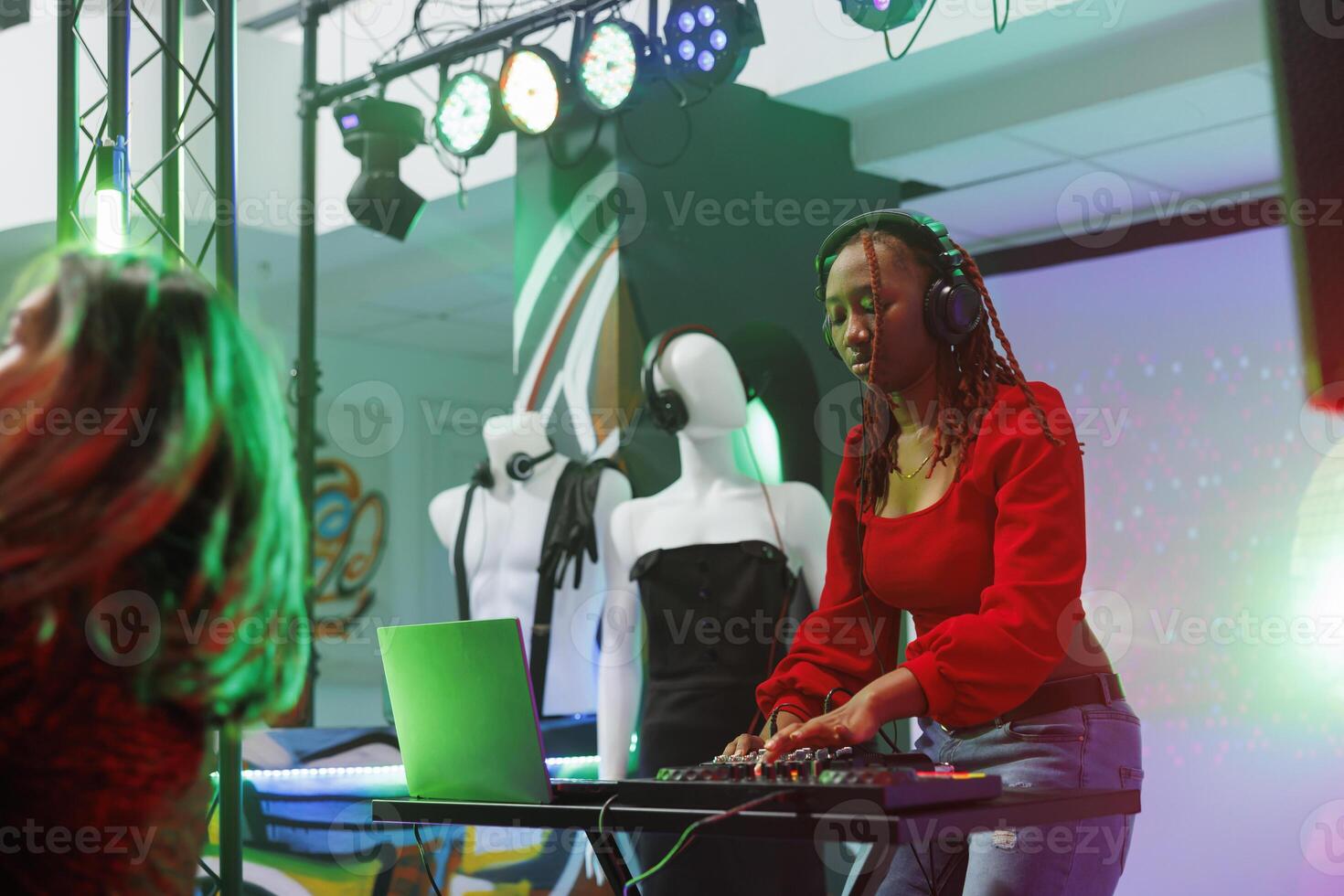 Musician using techno sounds mixer while performing on stage in nightclub. African american woman wearing headphones mixing music with dj station at disco party in club illuminated with spotlights photo