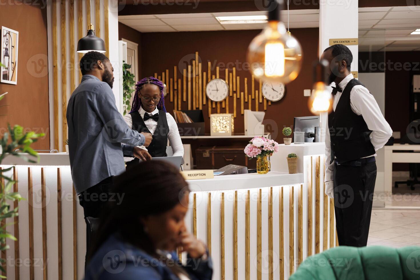 Friendly welcoming female receptionist helping tourist with check-in procedure at front desk. African American hotel staff assisting guest at reception, customer service in hospitality industry photo