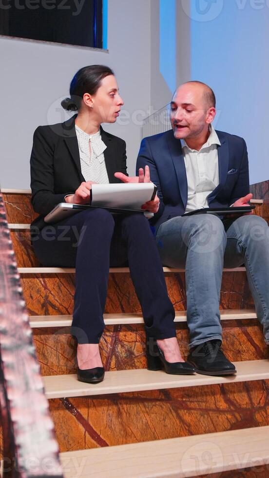 Tired overworked businesswoman arguing with colleague during difficult deadline sitting on staircase. Furious entrepreneur working in evening at corporate job explaining difficult finance project photo