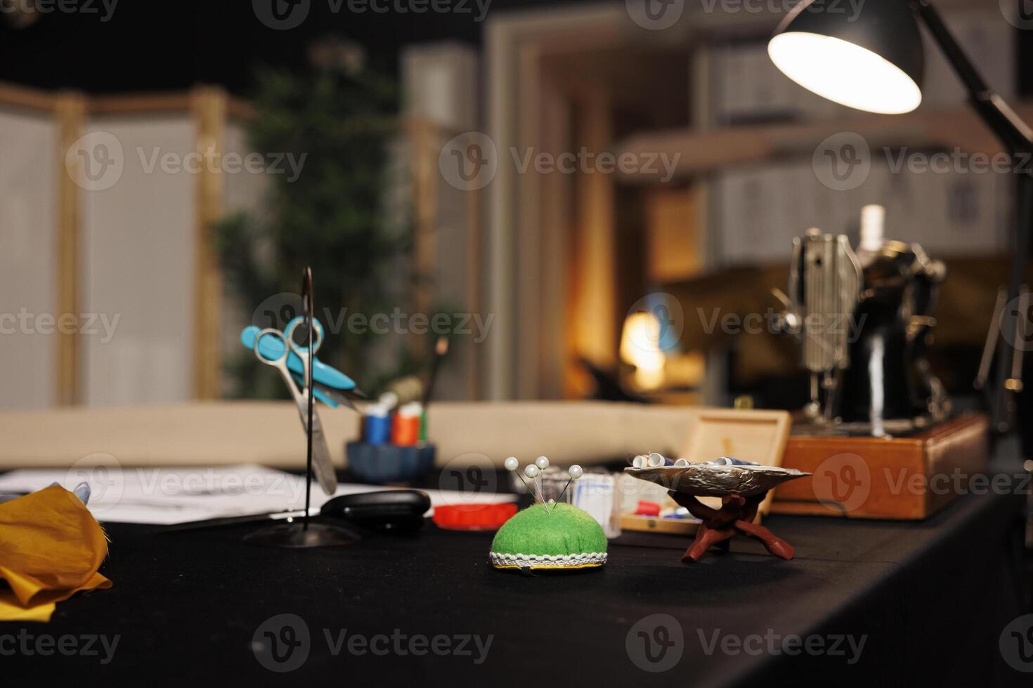 Scissors, sewing pins, needles, tailoring thread spools on table in atelier shop studio. Shot of professional dressmaking instruments used for manufacturing bespoke sartorial clothing photo