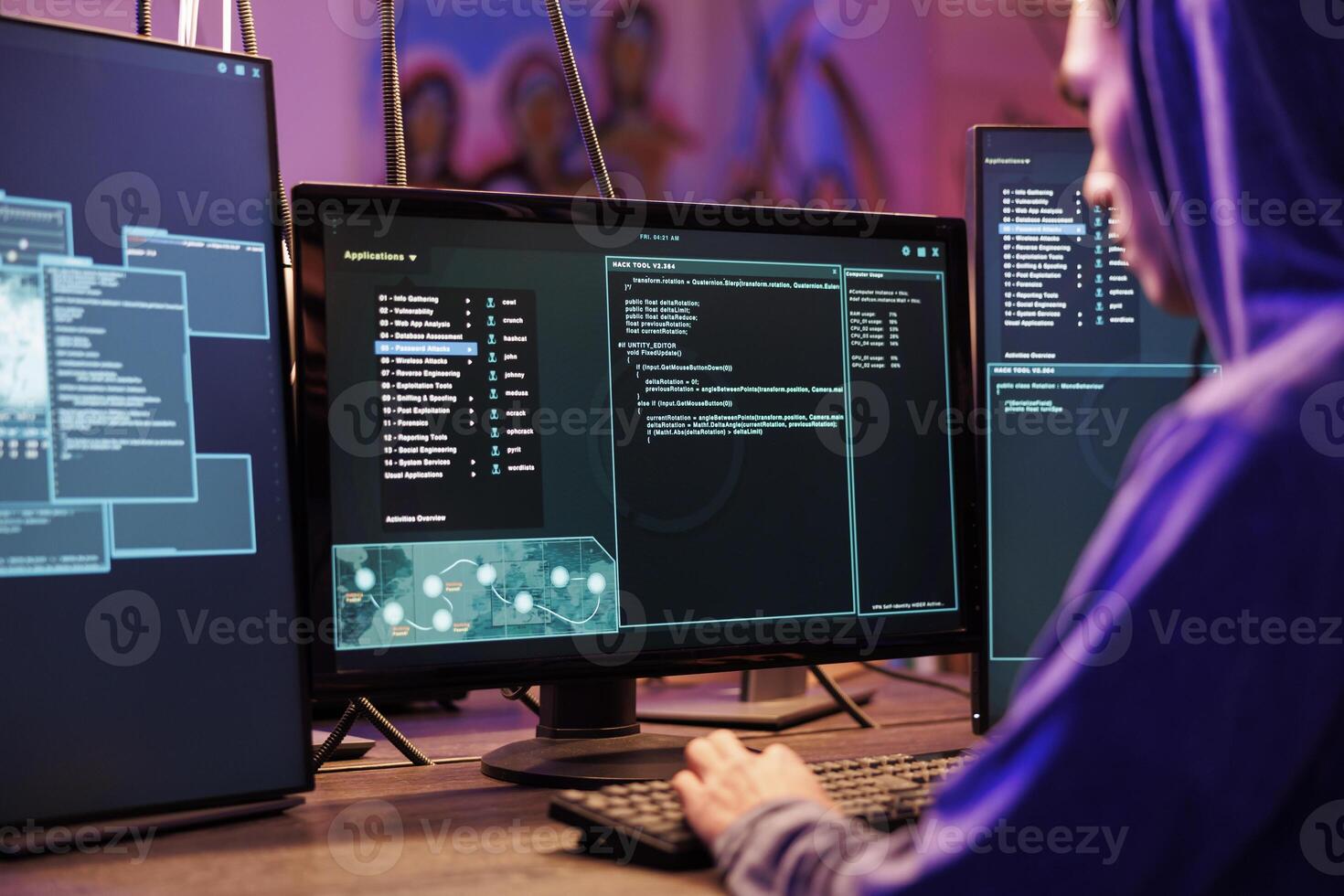 Hacker coding malicious software for password cracking in abandoned warehouse. Young man in hood programming illegal ransomware on computer with multiple monitors in hideout photo