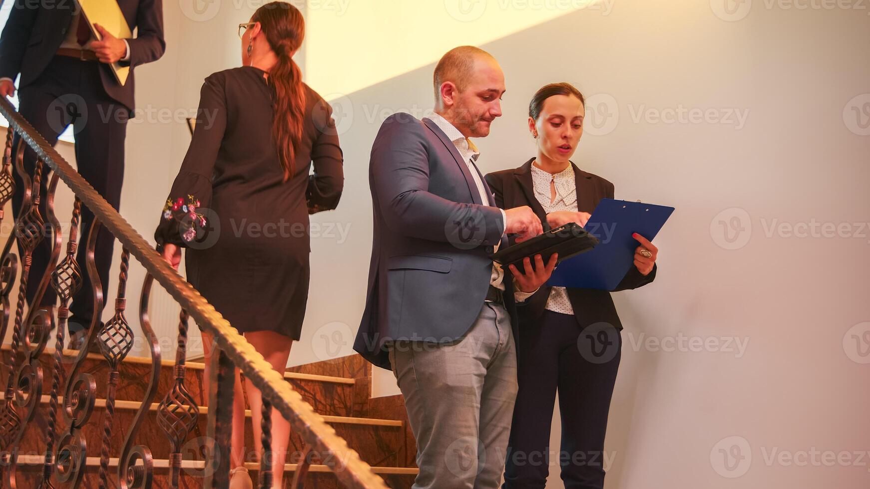 Business team walking on stairs meeting colleagues working using tablet, woman talking with corporate executive manager on staircase of business building. Entrepreneur overworking in office stairs. photo