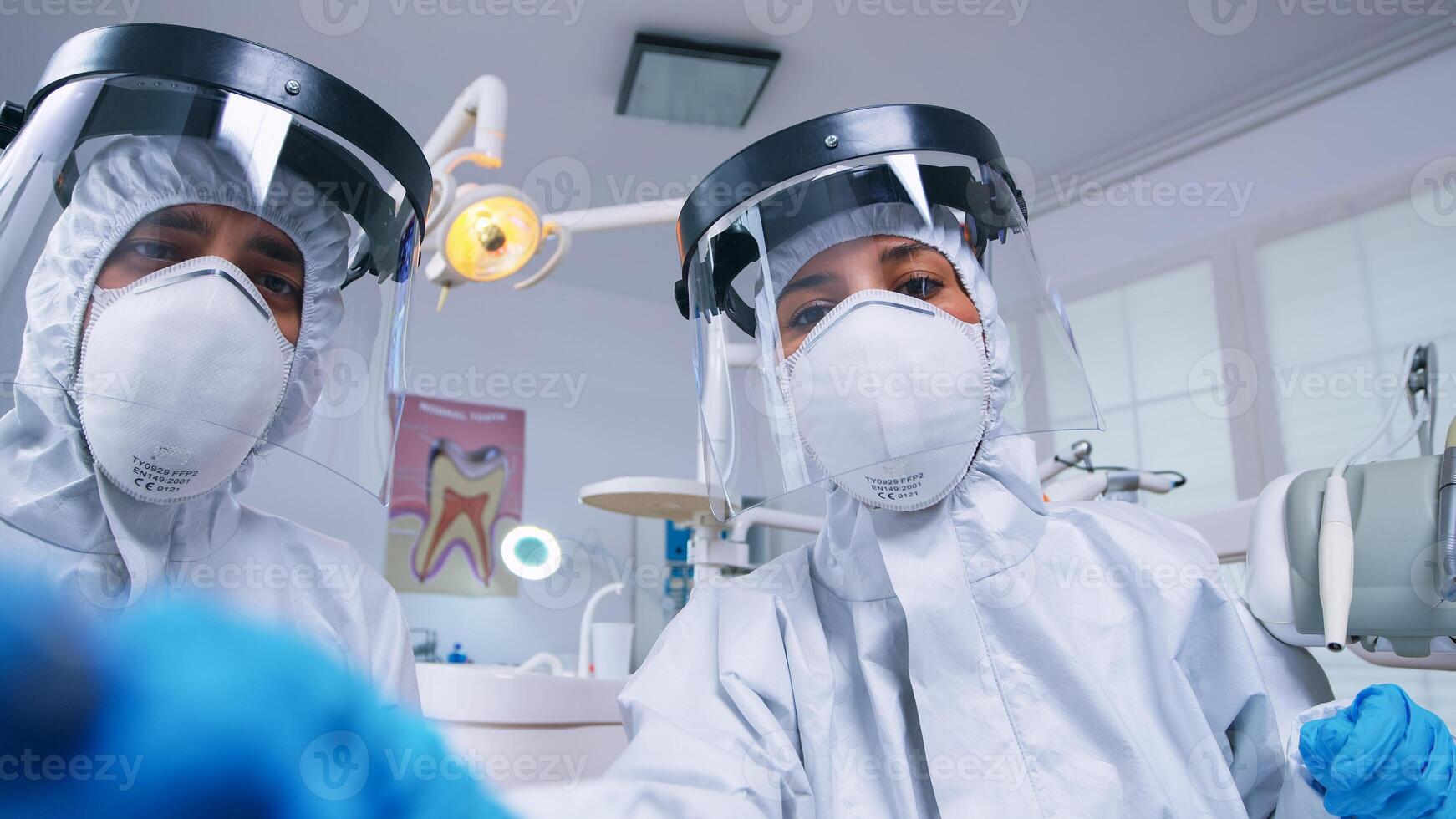 dental equipo propensión terminado paciente a trabajo en paciente cena vestido en materiales peligrosos traje en dental oficina con nuevo normal. estomatología equipo vistiendo la seguridad equipo en contra coronavirus tratando dientes problema. foto