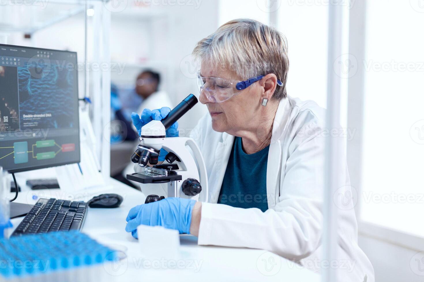 Senior scientist conducting scientific experiment with microscope. Elderly researcher carrying out scientific research in a sterile lab using a modern technology. photo