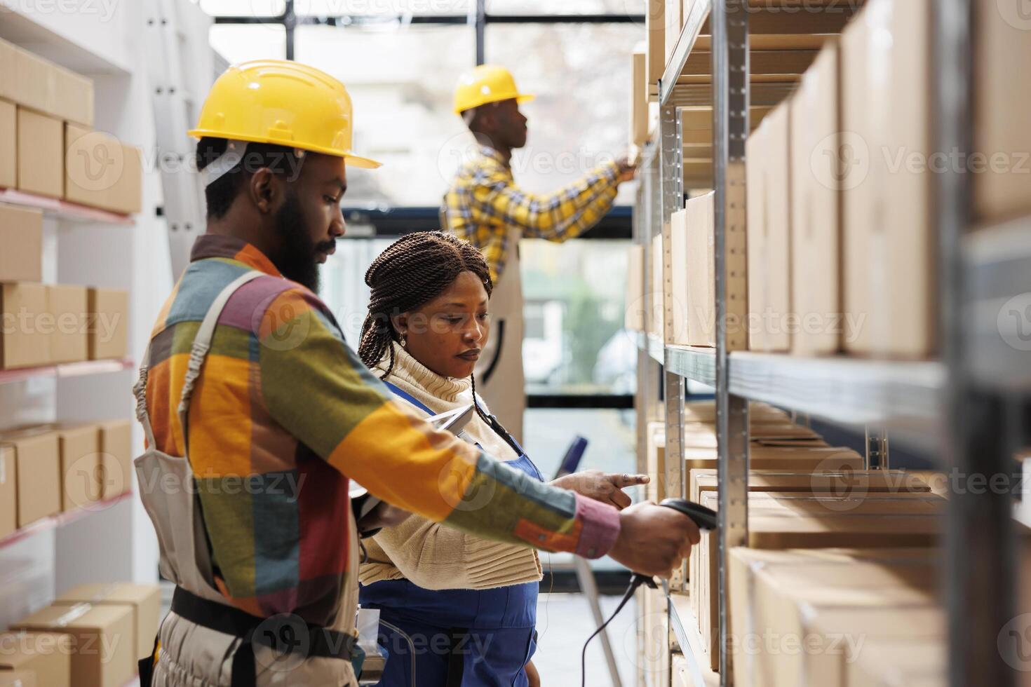 Warehouse manager supervising assistant scanning parcel barcode and pointing at cardboard box on shelf. African american storehouse worker using scanner on package and working with supervisor photo