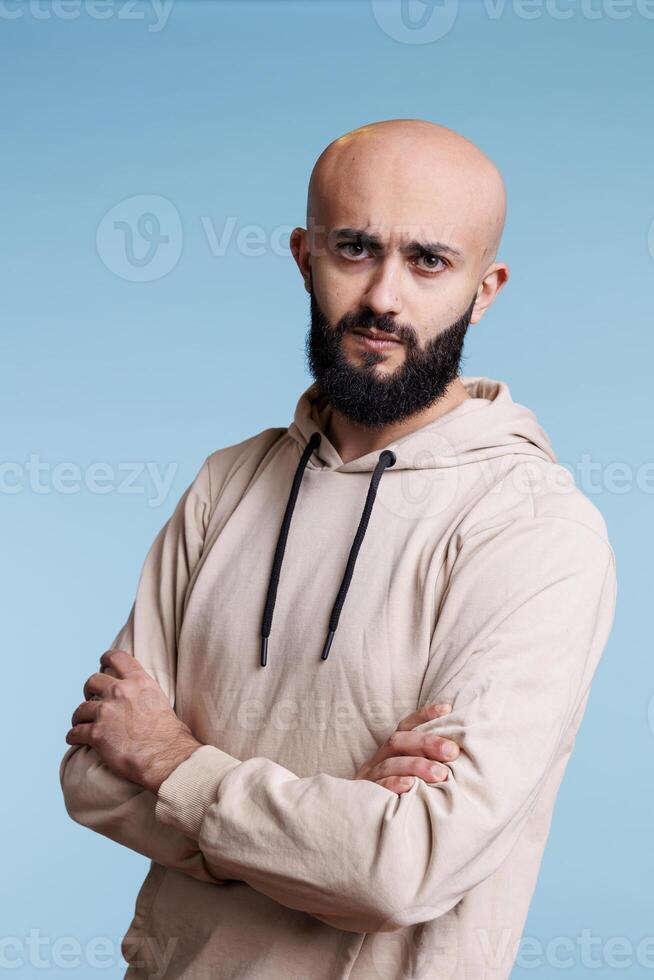 Serious arab man frowning eyebrows while posing with crossed arms studio portrait. Confused person with tensed facial expression standing with folded hands and looking at camera photo