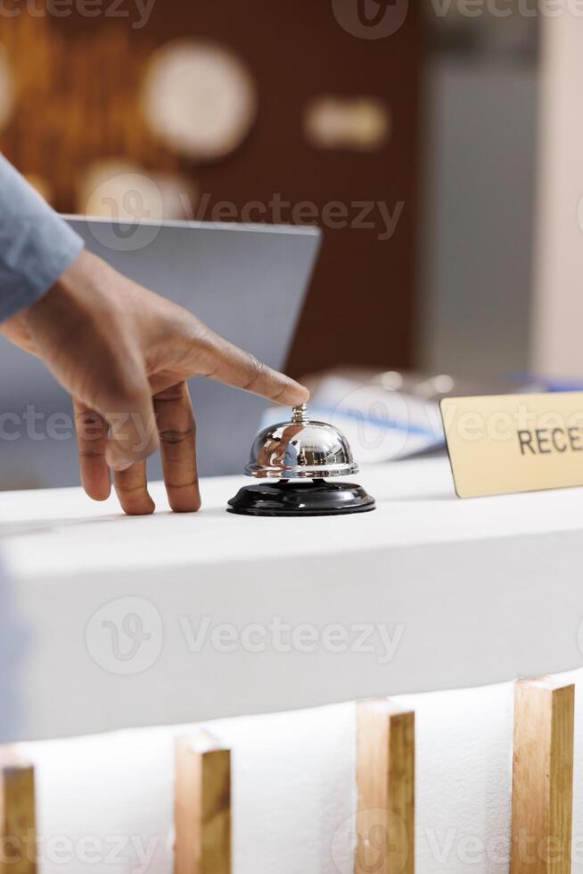 Close up of male hand pressing down front desk bell button while standing at empty reception counter, selective focus. Guest arrived at hotel, waiting for receptionist to check-in photo