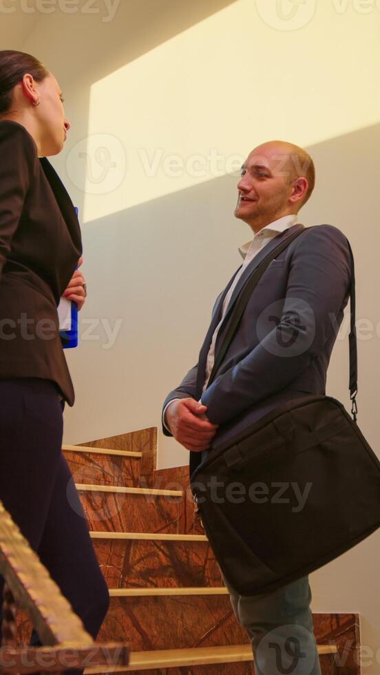 Businessman and attractive coworker standing on stairs talking and smiling in office corporate building. Group of professional successful businesspeople working together in modern financial workplace. photo