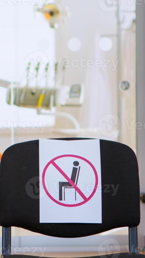 Empty waiting area, stomatology reception with nobody in it with new normal having sign on chair for social distance during covid-19 epidemic. Dental waiting room modern equipped in outbreak time photo