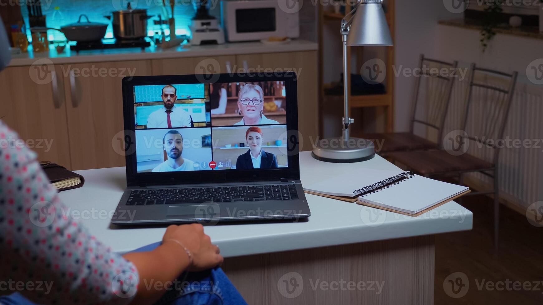 Woman talking with coworkers during video conference at midnight from home holding a cup of coffee. Lady using modern technology network wireless talking on virtual meeting at midnight doing overtime photo