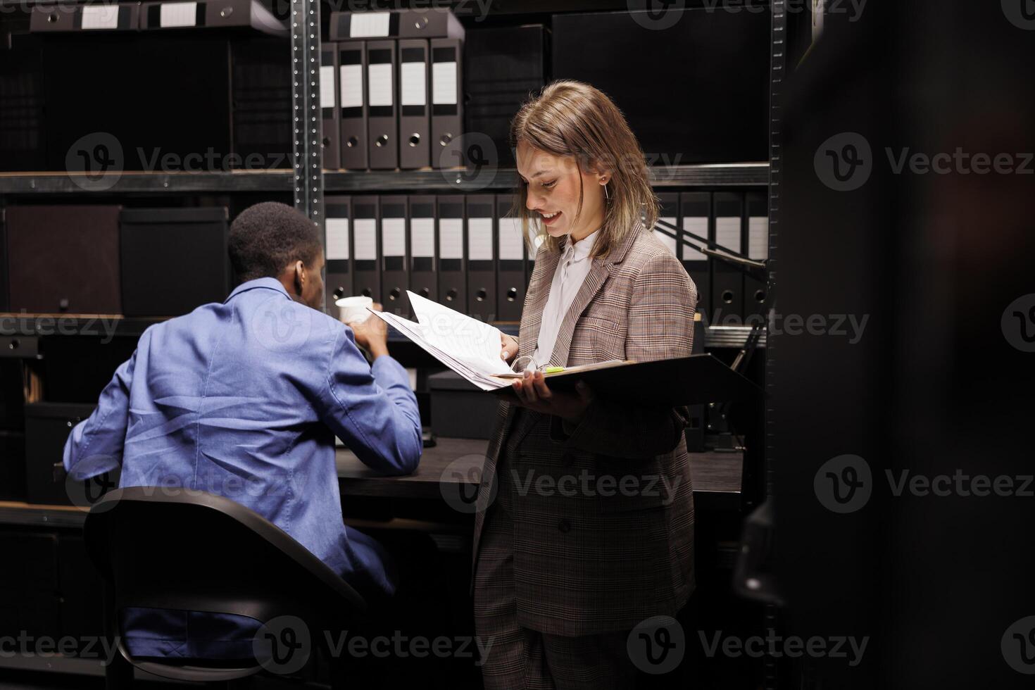 Workers discussing management report, analyzing administrative documents in corporate depository. Diverse employees reading bureaucracy record, discovering accountancy files in storage room photo