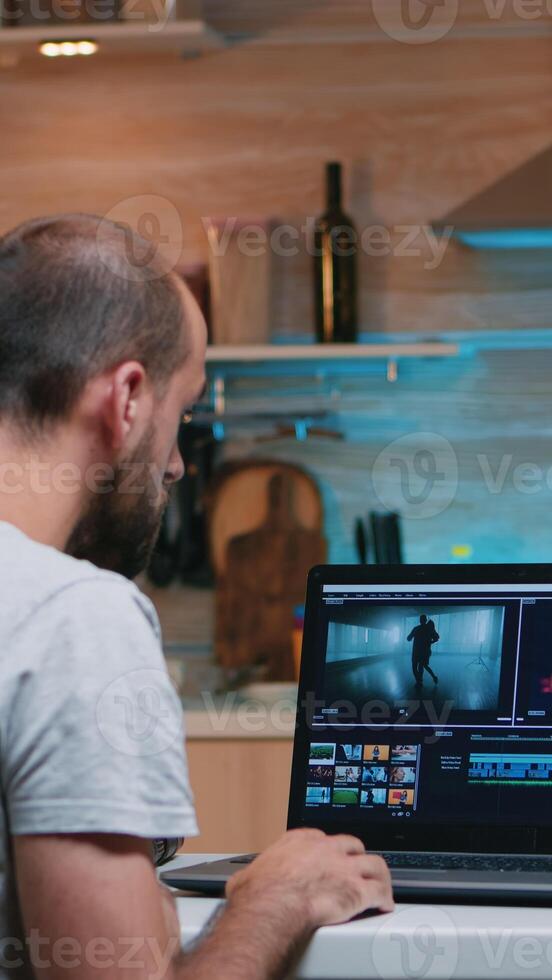 persona de libre dedicación edición un vídeo utilizando enviar producción software trabajando desde hogar tiempo extraordinario sentado en el cocina. camarógrafo Procesando audio película montaje en profesional ordenador portátil tarde a noche foto