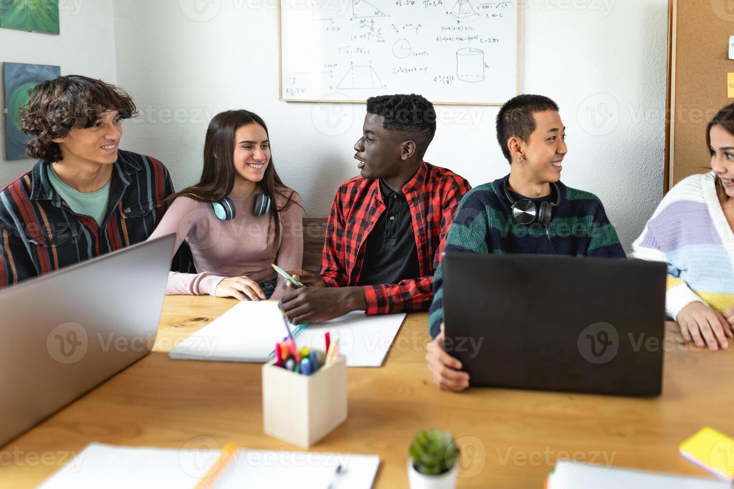 Young multiracial students reading books and using laptop in classroom while studying together - School education concept photo