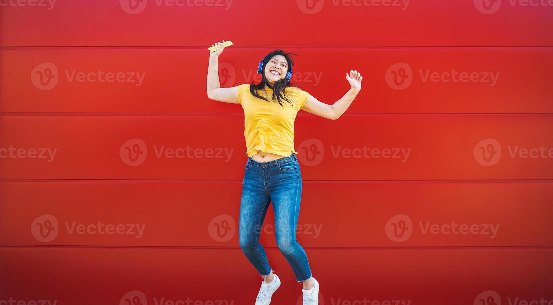 Happy Asian girl jumping while listening music playlist with wireless headphones - Young woman having fun dancing outdoor - Youth millennial generation lifestyle people and technology concept photo
