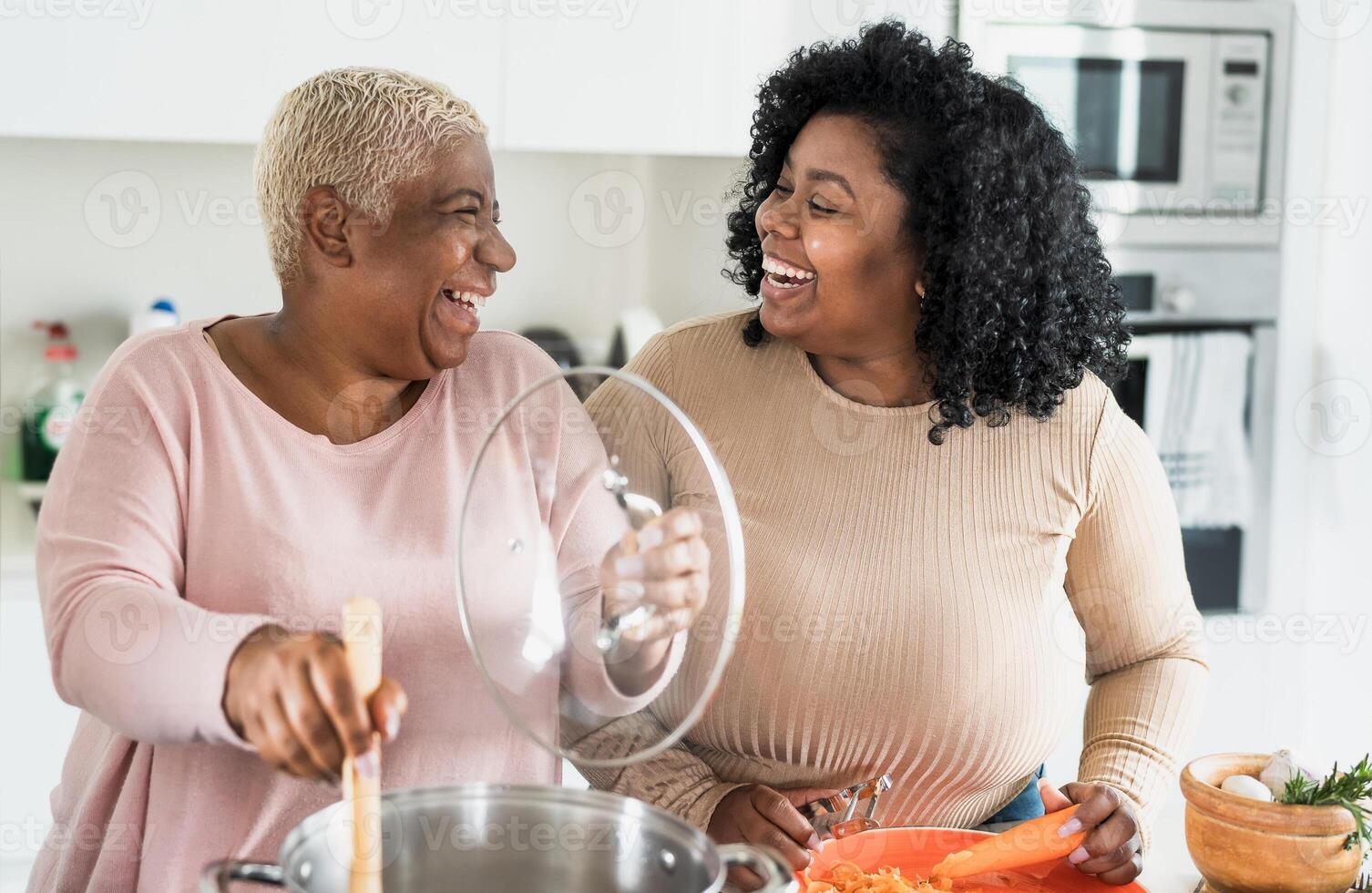 Happy Afro mother and daughter preparing lunch together in modern house kitchen - Food and parents unity concept photo