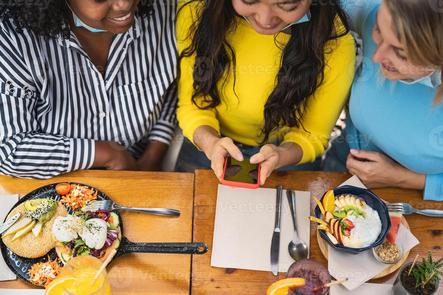 multirracial amigos acecho en móvil teléfono inteligente mientras teniendo sano almuerzo en café desayuno tardío bar durante corona virus brote - comida y tecnología concepto foto