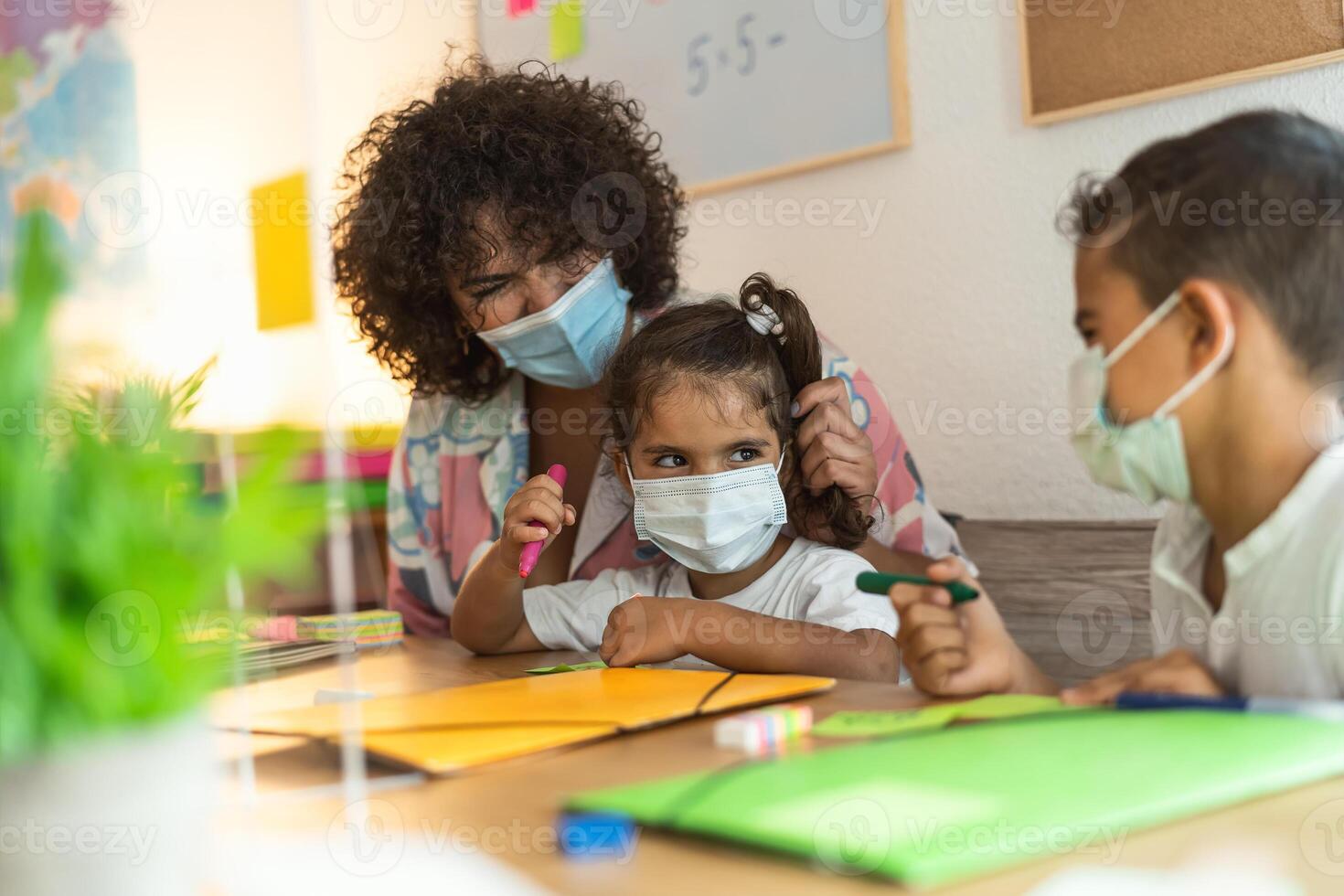 Teacher with children wearing face mask in preschool classroom during corona virus pandemic - Healthcare and education concept photo