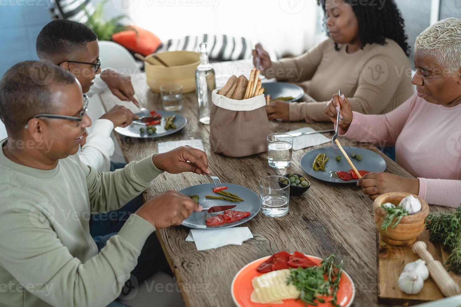 Happy afro Latin family eating healthy lunch with fresh vegetables at home - Food and parents unity concept photo