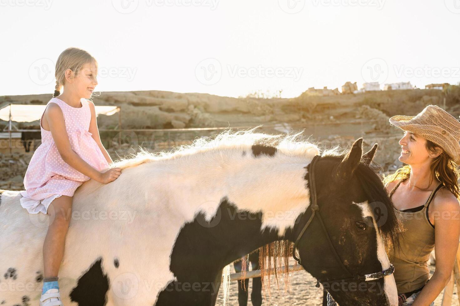 Happy farmer family mother and daughter having fun riding horse inside ranch photo