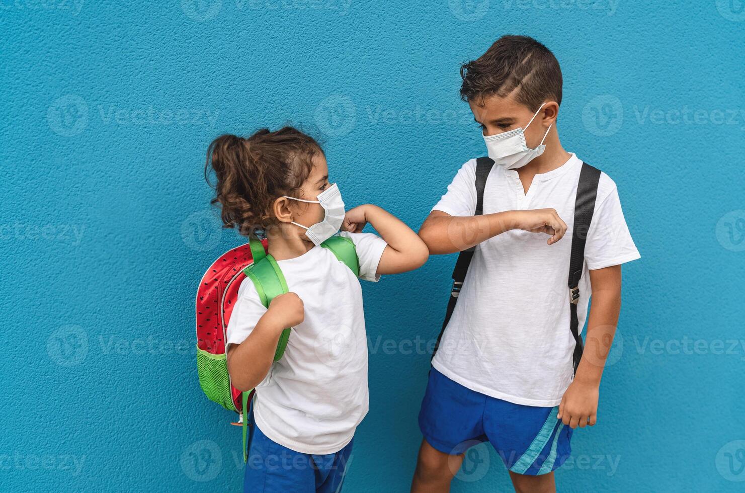 niños vistiendo cara protector máscara yendo espalda a colegio durante corona virus pandemia - pequeño niños haciendo nuevo social distancia saludo golpeando codos - cuidado de la salud y educación concepto foto