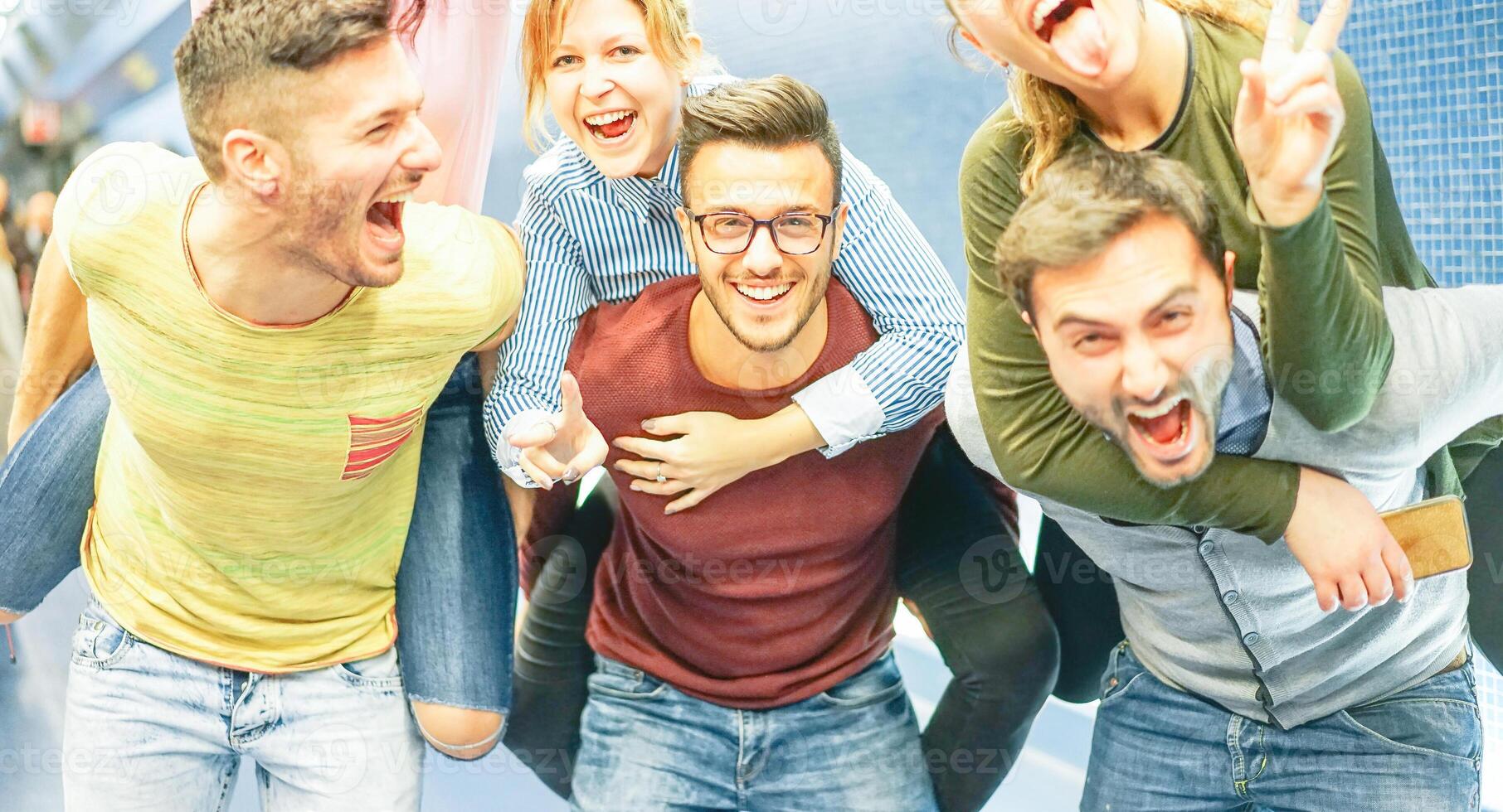 Group of friends having fun in a underground station - Men piggybacking their girlfriends - Young people making party - Concept of friendship, lifestyle and youth photo