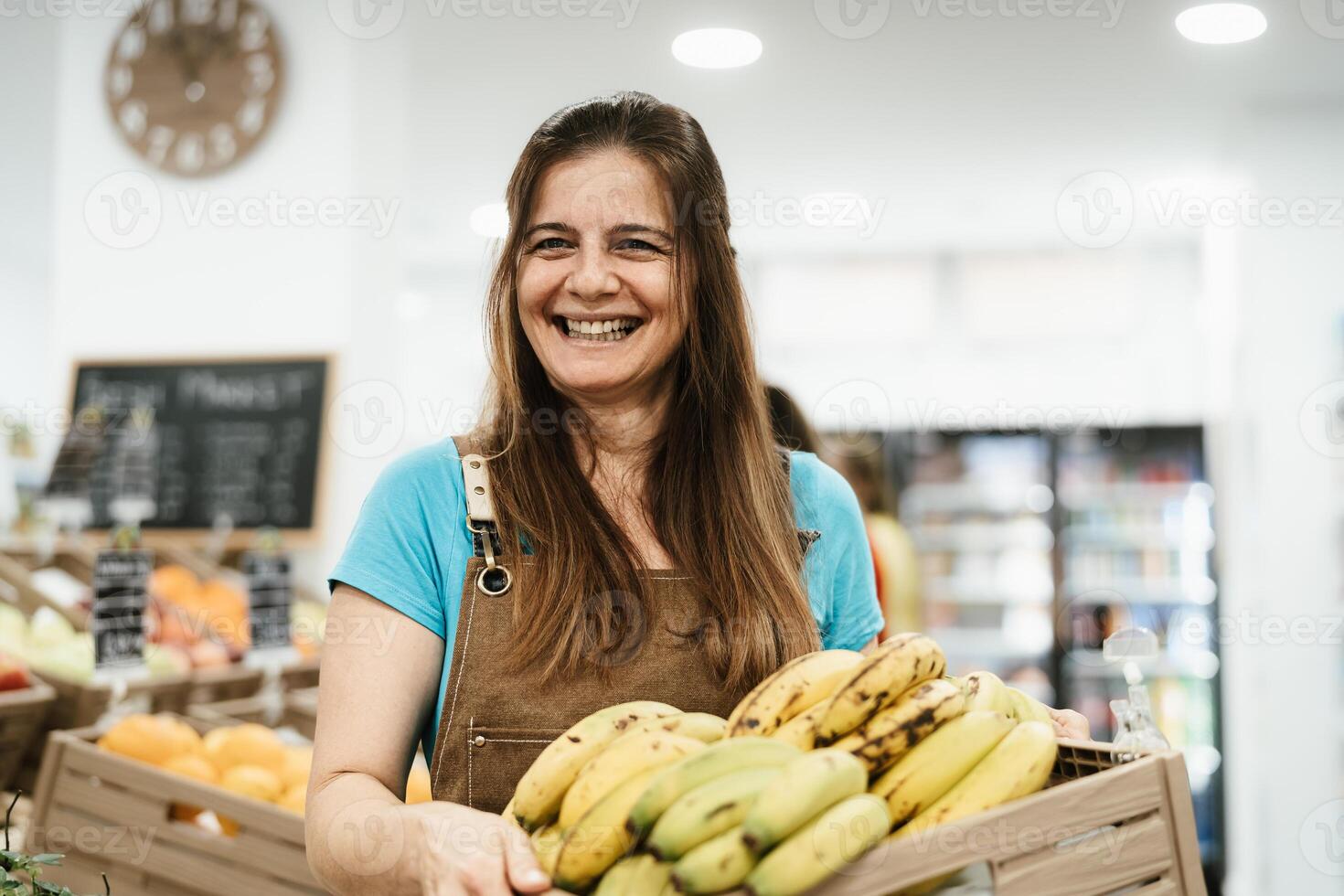 Happy woman working inside supermarket holding a box containing fresh bananas photo