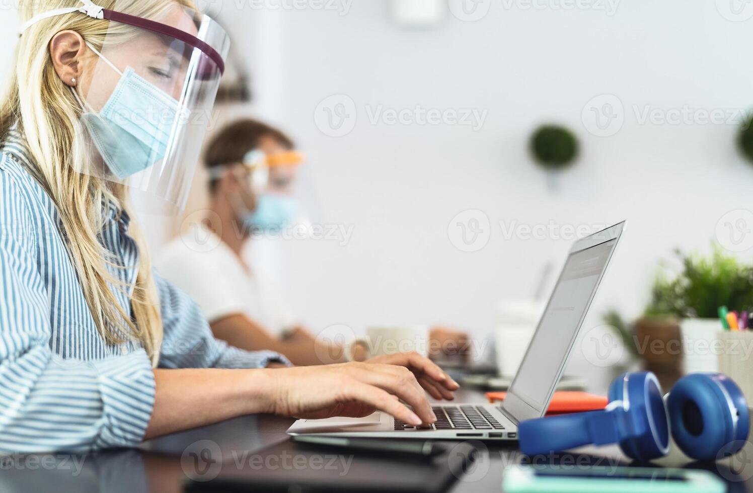 Young people working in co-working creative space wearing surgical mask protection for preventing corona virus spread - Social distancing, content creator startups and technology concept photo