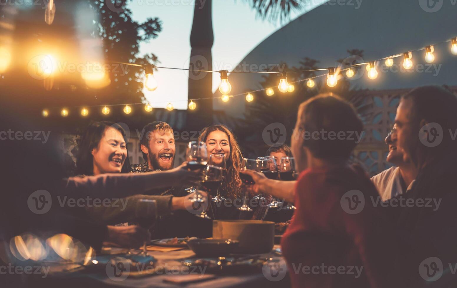Happy family dining and tasting red wine glasses in barbecue dinner party - People with different ages and ethnicity having fun together - Youth and elderly parents and food weekend activities concept photo