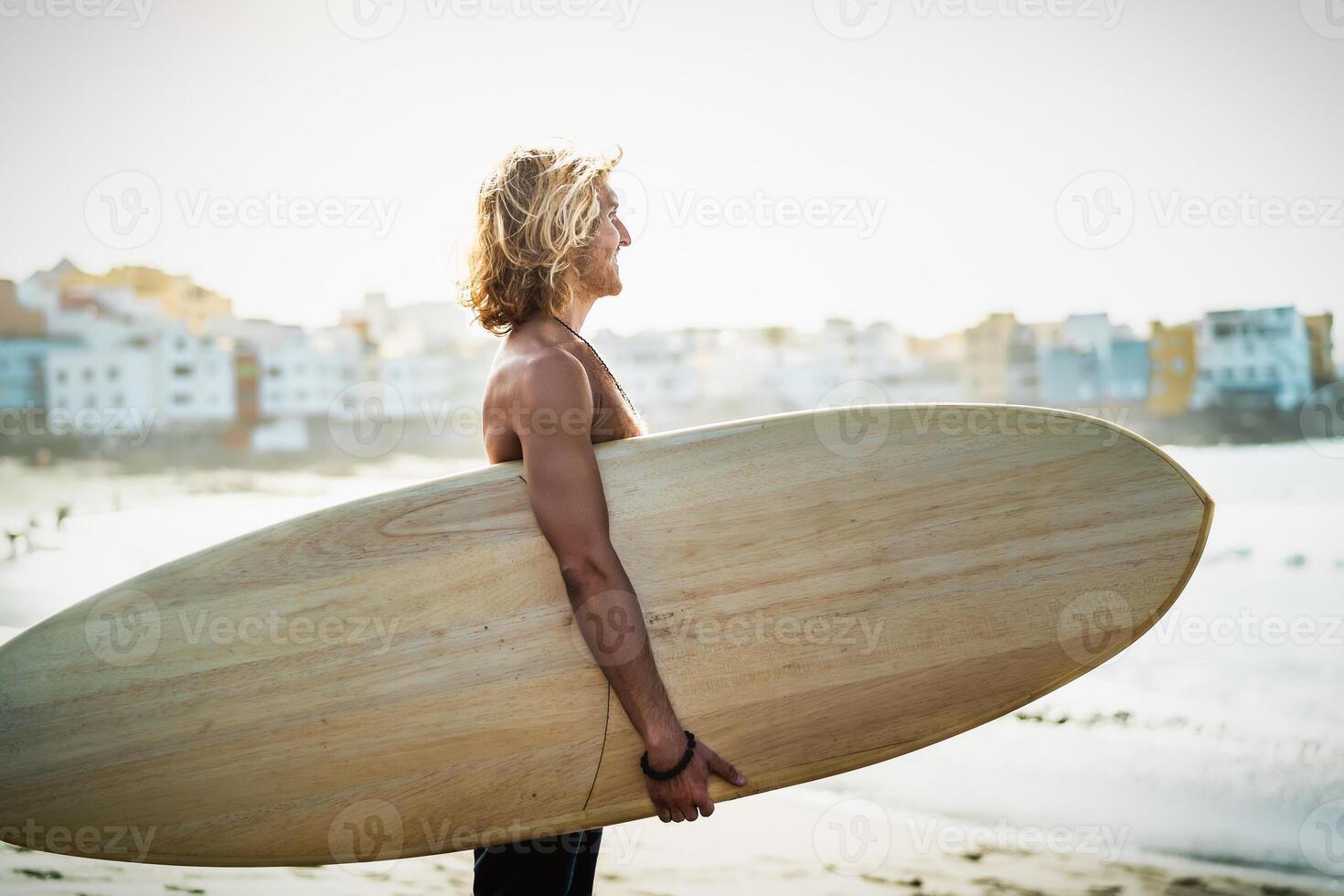 Fit young man having fun surfing during sunset time - Happy surfer male holding surfboard on the beach - Youth people lifestyle and extreme sport concept photo