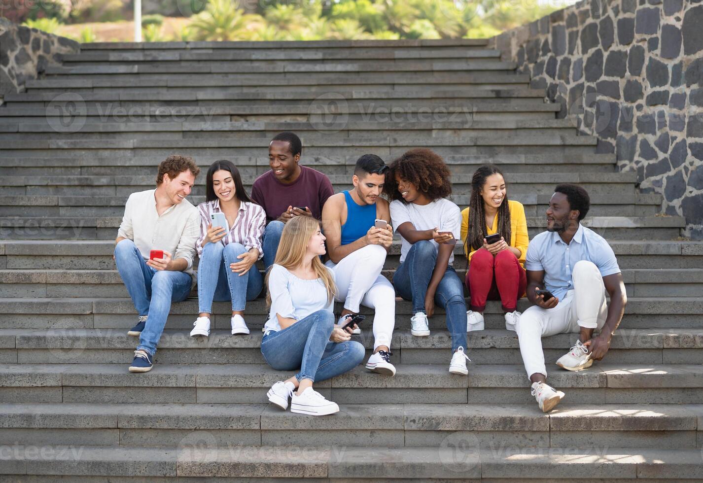 joven multirracial grupo de amigos utilizando móvil teléfono inteligente sentado en escalera fuera de Universidad - juventud milenario estilo de vida concepto foto