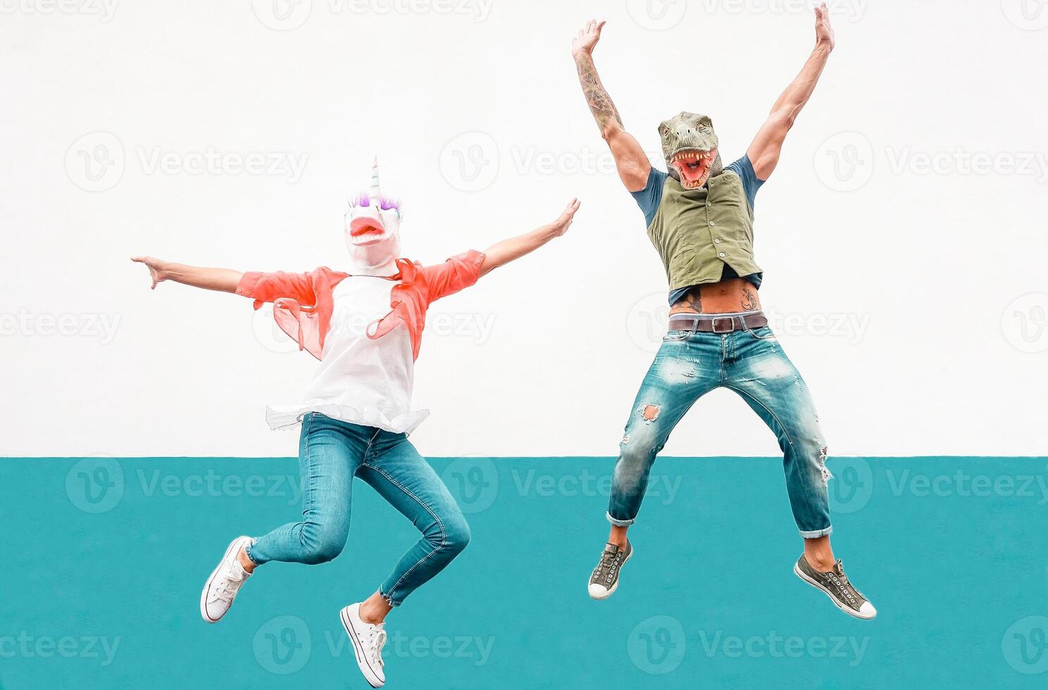 Happy seniors crazy couple wearing unicorn and t-rex mask while jumping outdoor - Mature trendy people having fun celebrating outside - Absurd concept of masquerade funny holidays photo