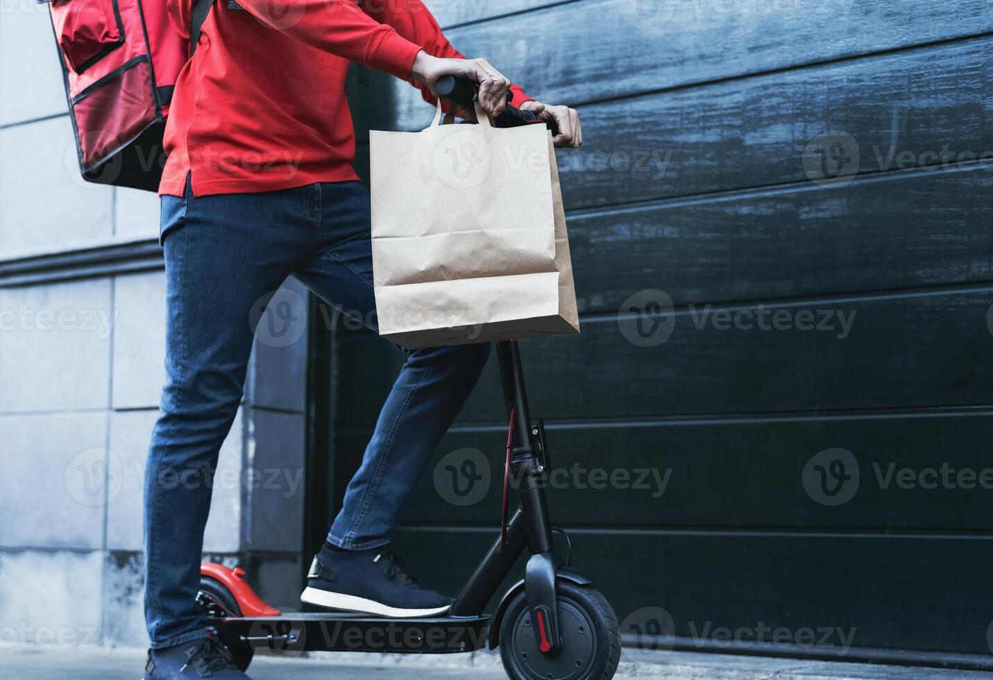 Rider man delivering meal to customers house with electric scooter - Ecological fast delivery food concept - Focus on trousers photo